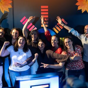 Photographie d’un groupe d’entreprise posant joyeusement devant un mur noir comportant le logo Musi'Quiz
