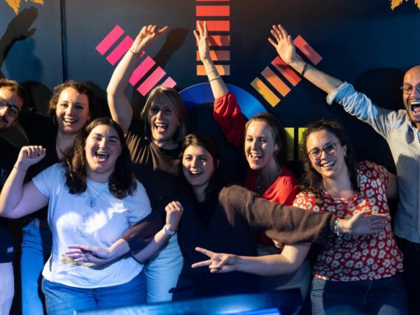 Photographie d’un groupe d’entreprise posant joyeusement devant un mur noir comportant le logo Musi'Quiz