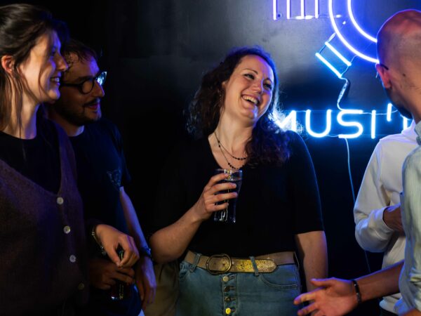 Groupe de personnes qui rient dans une salle Musi’Quiz, sur fond noir, avec le logo Musi’Quiz.