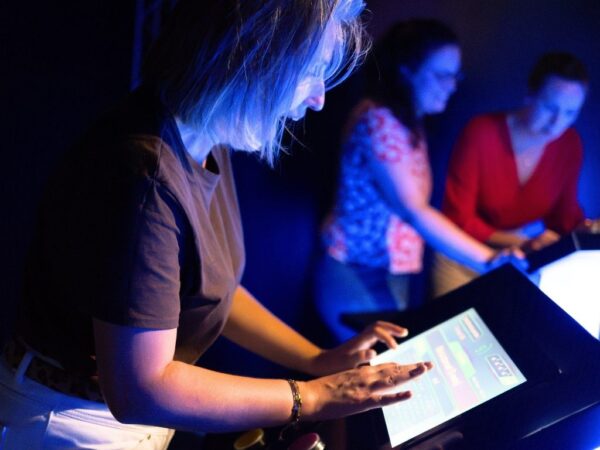 Joueuse concentrée en train de compléter les paroles sur un buzzer tactile immersif lors d’un défi musical. L’ambiance lumineuse et les écrans interactifs plongent les participants dans une expérience digne d’un plateau TV.